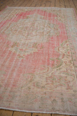 Worn pile and faded cherry red, blush, ivory hues on distressed Oushak rug corner.