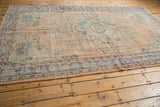 Distressed corner of Oushak rug with intact side selvage, faded beige and blue pattern.
