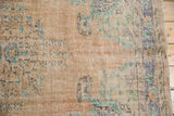 Distressed Oushak carpet featuring textured wear on soft beige with faded blue and mint green motifs.