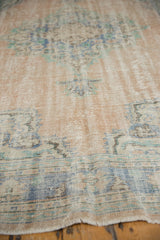 Worn fringe and faded blush, blue patterns of a distressed Oushak rug.
