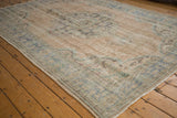 Distressed vintage Oushak carpet surface showing worn beige pile, faded seafoam green, and charcoal floral patterns.