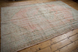 Distressed Oushak carpet edge showing blush pink, seafoam green, and wear to knot heads.