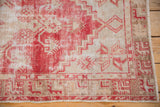 Distressed Oushak rug corner showing pale red and beige geometric patterns, wear, corded selvage.