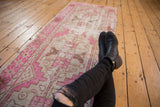 Distressed Oushak runner showing worn pile, fuchsia, ivory, and coffee brown geometric patterns.