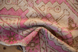 Close-up of distressed Oushak rug pile with fuchsia, beige, and brown stepped patterns.