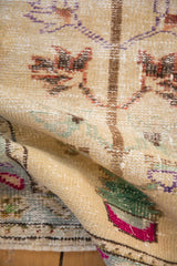 Textured fold of vintage distressed Oushak rug shows fuchsia and emerald floral designs.