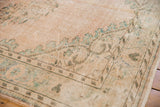 Worn texture and faded green vinery on the beige field of a distressed Oushak rug.