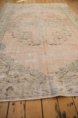 Distressed pile texture with faded green motifs on the secured end of vintage Oushak rug.