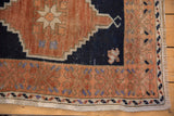 Distressed Oushak rug corner: textured copper border with bursting blossoms, navy field, and fringe.