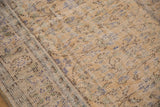 Distressed Oushak carpet close-up, faded pale gold and blue vinery, foundation visible.