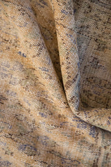 Folded pile of distressed Oushak rug showing soft texture, faded gold, blue, green.