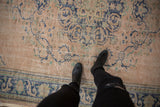 Distressed vintage Oushak rug pile, featuring faded cobalt blue scrolling arabesques on dusty rose.