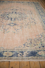 Distressed vintage Oushak rug corner with dusty rose field, cobalt blue border, and fringe.