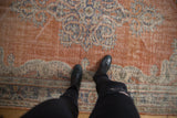 Distressed Oushak rug showing burnt orange abrashed field, ornate blue vinery, and surface wear.