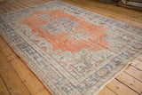 Distressed Oushak rug corner shows worn orange abrashed field and stylized blue-ivory border.