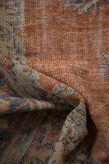Folded distressed Oushak rug with burnt orange pile, visible knot heads, and dusty blue.