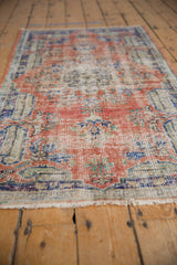 Distressed Oushak rug: worn pile texture, madder red, blue, ivory floral motifs, visible foundation.