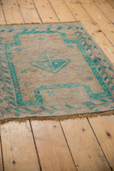 Angled view of distressed Oushak rug, emerald geometric motifs on beige, wear to knot heads.