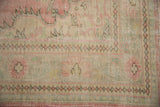 Distressed Oushak rug corner with faded pink, ivory, seafoam geometric patterns.