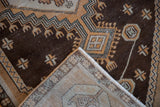 Distressed Oushak rug corner showing chocolate brown geometric pile and woven ivory foundation.