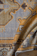 Folded vintage distressed Oushak rug texture with saffron yellow, pale blue, and chocolate brown geometric motifs.