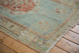 Distressed corner of vintage Oushak rug, showing worn pile, fringe, and floral borders.