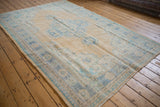 Distressed Oushak carpet corner with pale saffron field, faded blue border, and visible foundation.