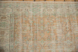 Distressed vintage Oushak rug corner, showing worn apricot, ivory, and sea foam floral patterns.