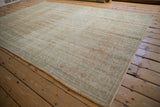 Distressed Oushak rug corner, visible wear, pale apricot and mint green scrolling motifs.