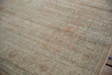 Distressed Oushak rug close-up showing worn pile, subtle scrolling tendrils, muted apricot and mint green.
