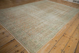 Distressed Oushak rug corner, showing wear, pale apricot and mint floral tendrils on ivory.