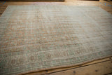 Distressed Oushak rug edge, faded terra cotta, mint scrolling tendrils, visible knot heads.