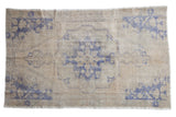 Distressed vintage Oushak rug featuring a faded pale blue medallion and spandrels on a light beige field.