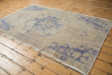 Distressed Oushak rug corner with worn beige pile and faded blue spandrel motif.