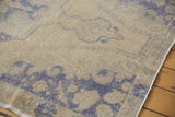 Faded blue curvilinear motifs on distressed beige Oushak rug, showing even wear and subtle foundation.