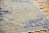 Distressed corner of a vintage Oushak rug with faded pale blue motifs on a beige field.