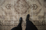 Distressed vintage Oushak rug showing worn texture, ivory and chocolate brown patterns.