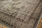Distressed Oushak rug showcasing brown geometric and botanical border patterns.