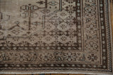 Distressed Oushak rug corner with faded floral motifs, chocolate brown border, and fringe.