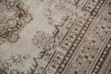 Distressed Oushak carpet texture, showing faded plant motifs in antique ivory, chocolate brown, and silver.