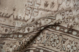 Folded Oushak rug with distressed texture, showing worn knot heads, beige and brown patterns.