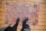Distressed Oushak rug corner showing worn seed motif, pink, ivory, and plum colors.