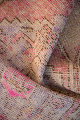 Visible foundation and texture on a folded distressed Oushak rug with soft pinks and purples.