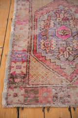 Distressed Oushak rug corner revealing wear, pink-purple tones, and intact side selvage.