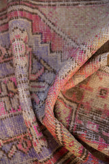 Distressed textured pile of a vintage Oushak rug in faded pink, plum, and brown.