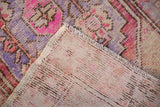 Hand knotted Oushak rug corner, showing distressed purple and pink pile with foundation.