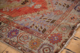 Vintage Oushak rug corner with abrashed lilac-blue border, rust field, lily petal spandrel, and wear.