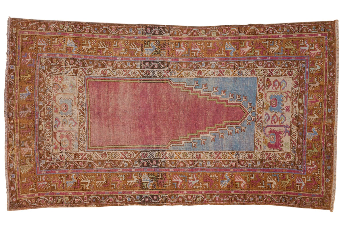 Distressed Turkish Oushak rug with a prayer design in faded purple, sky blue, and saffron yellow.