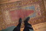 A personal view showing the scale of a distressed Oushak rug with a purple and blue prayer design.