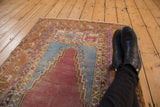 Colorful vintage Oushak prayer rug with distressed wear, viewed from a personal angle.